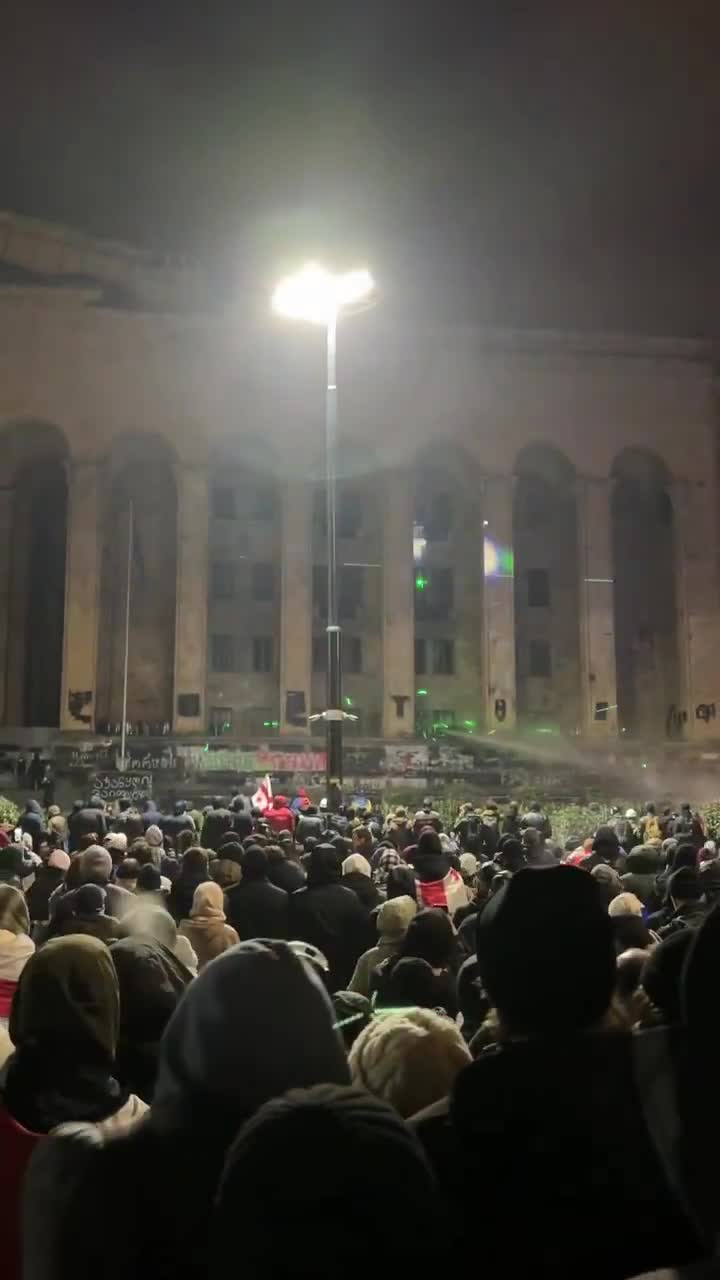 Protesters launch fireworks toward the Georgian parliament building, where riot police are deployed on the stairs. The riot police are firing water cannons back at the gathered demonstrators