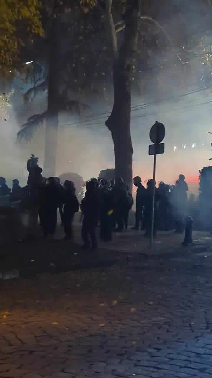 Riot police are facing groups of protesters from two sides. Protesters fire fireworks while police shoot tear gas grenades. Nini Gabritchidze/Civil.ge