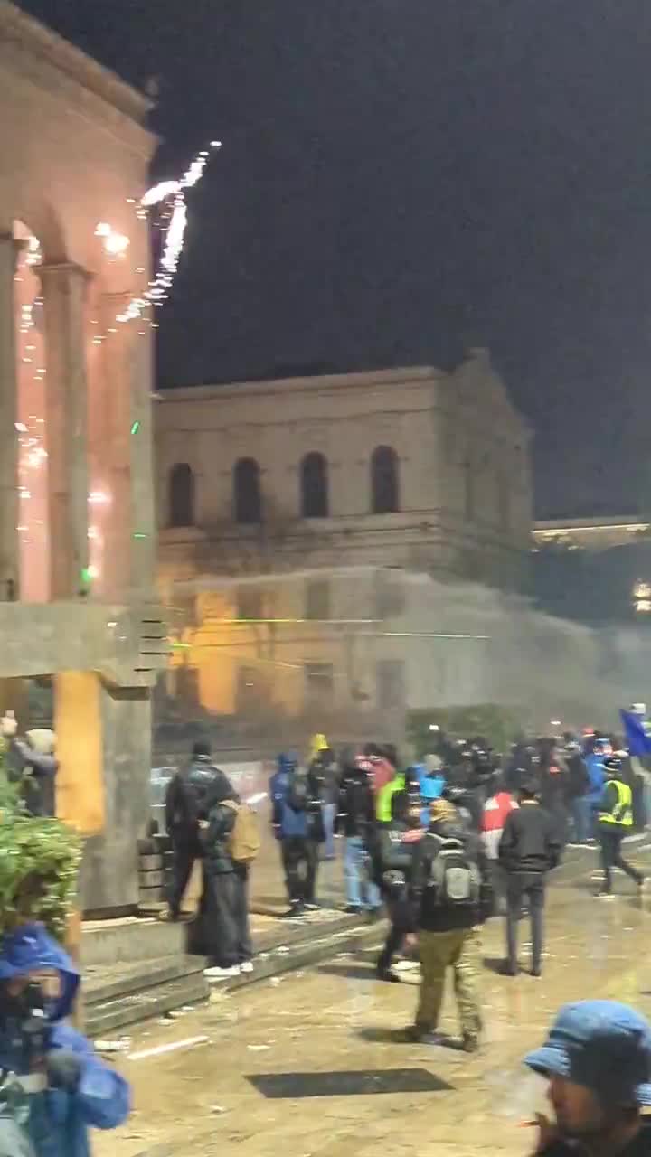 Riot police again pouring streams of water at protesters from inside the parliament. Water cannons also mobilized, and protesters occasionally fire fireworks at the parliament