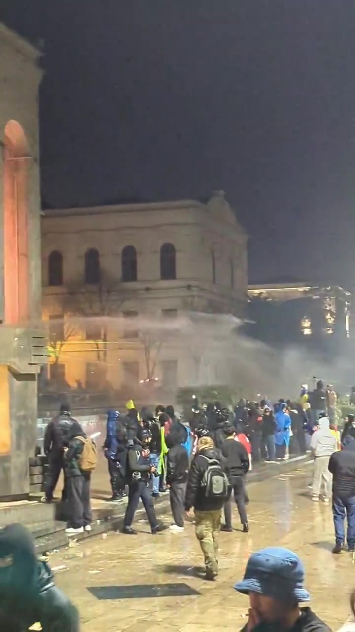 Riot police again pouring streams of water at protesters from inside the parliament. Water cannons also mobilized, and protesters occasionally fire fireworks at the parliament